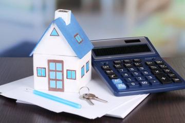 Small house and calculator on table close-up to estimate value